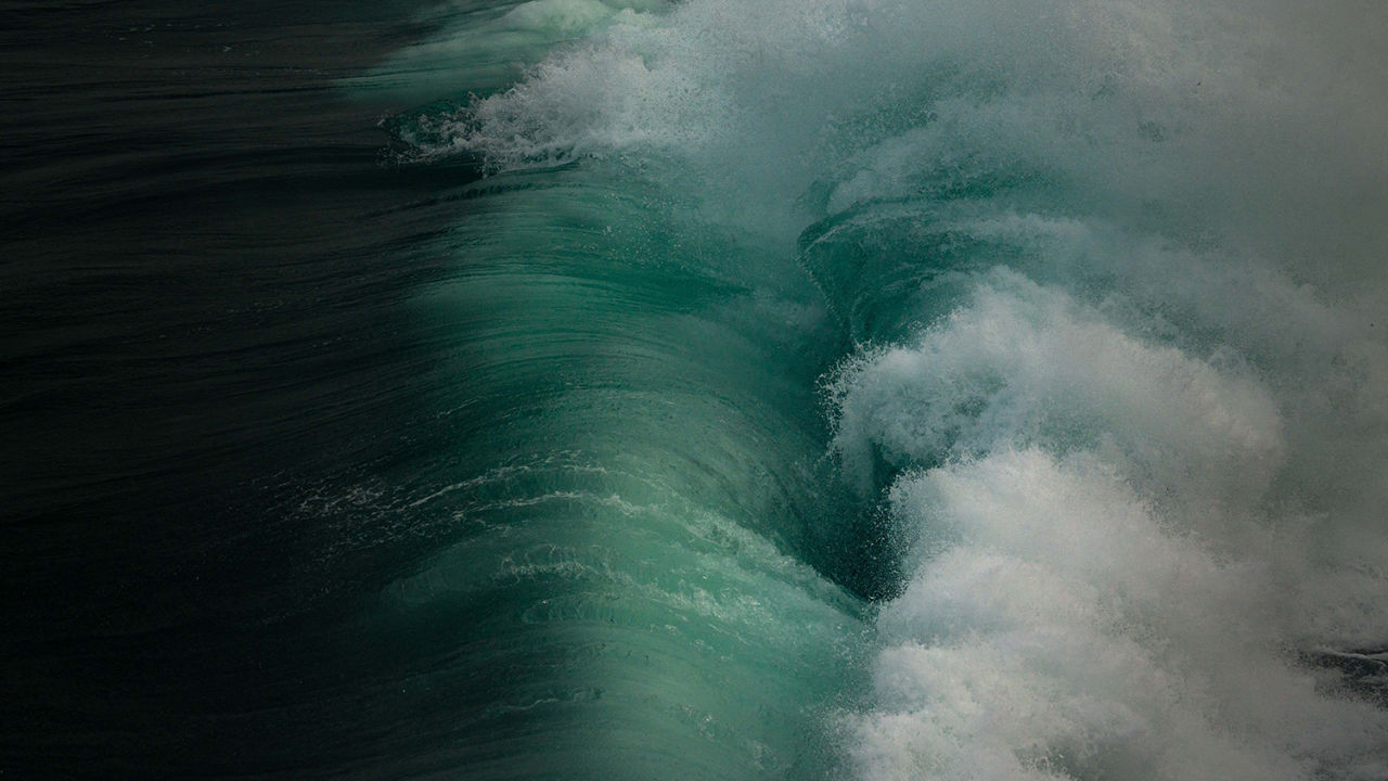 An aerial shot of a large wave crashing on to the ocean's surface causing whitewash.